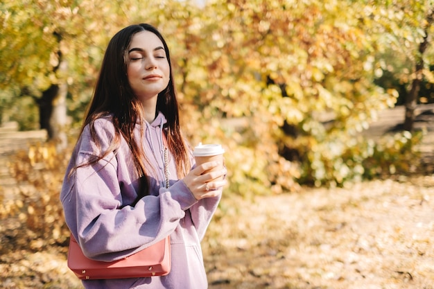 Schöne junge Frau, die Kaffee trinkt und Herbstwetter im Park genießt.