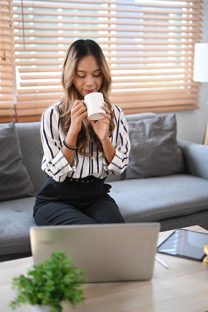 Schöne junge Frau, die Kaffee trinkt, während sie Freizeit zu Hause verbringt