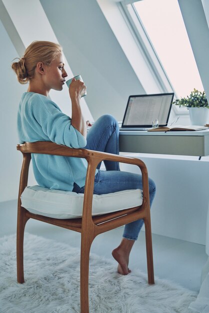 Schöne junge Frau, die Kaffee trinkt, während sie zu Hause arbeitet