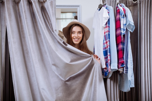 Schöne junge Frau, die Kleidung in der Umkleidekabine des Bekleidungsgeschäfts anprobiert