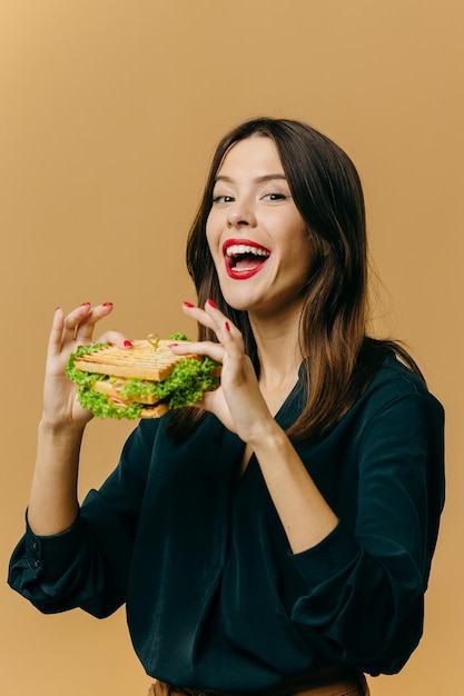 Schöne junge Frau, die mit einem Sandwich auf einem farbigen Hintergrund aufwirft