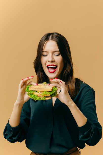 Schöne junge Frau, die mit einem Sandwich auf einem farbigen Hintergrund aufwirft