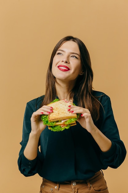 Schöne junge Frau, die mit einem Sandwich auf einem farbigen Hintergrund aufwirft