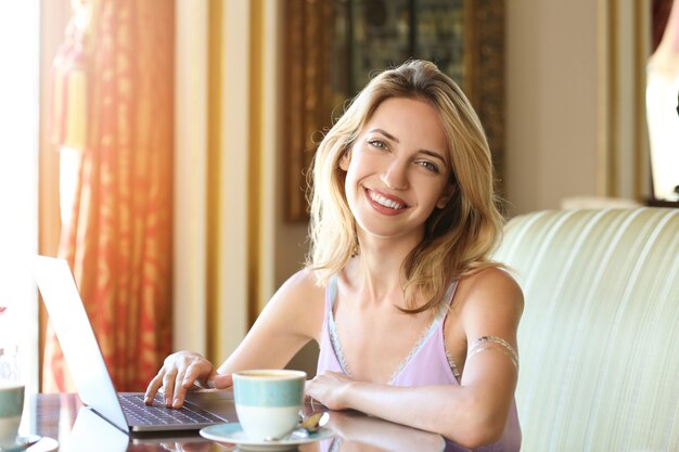 Schöne junge Frau, die mit Laptop arbeitet und Kaffee im Café trinkt