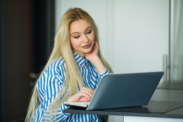 schöne junge Frau, die mit Laptop zu Hause in der Küche arbeitet