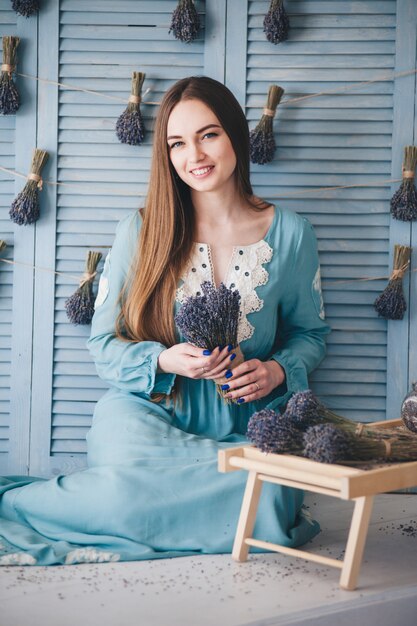 Schöne junge Frau, die mit Lavendel gegen die blaue Wand sitzt.
