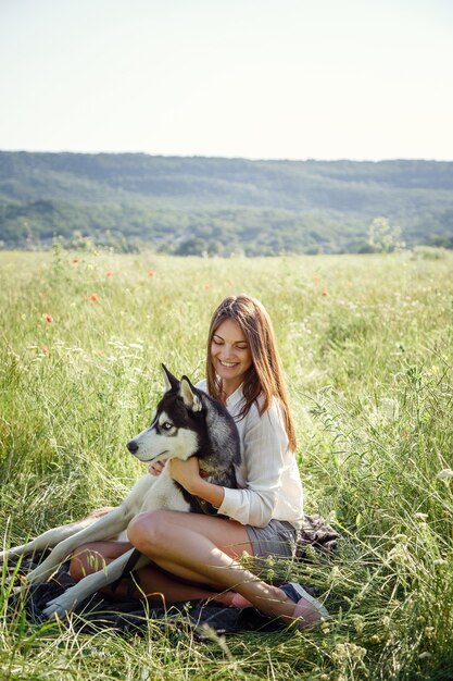 Schöne junge Frau, die mit lustigem Huskyhund draußen im Park spielt