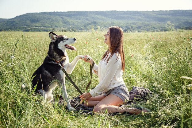 Schöne junge Frau, die mit lustigem Huskyhund draußen im Park spielt