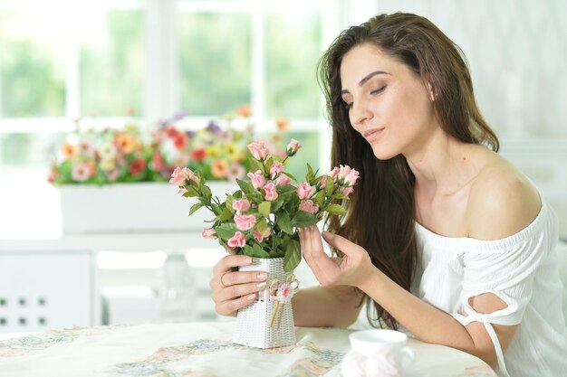 Schöne junge Frau, die mit schönen rosa Rosen am Tisch sitzt