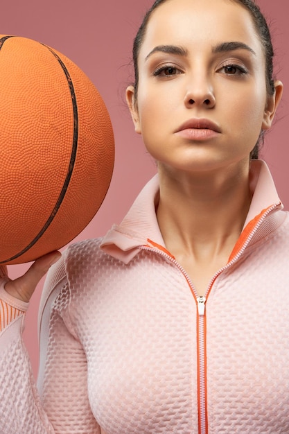 Schöne junge Frau, die orange Basketballball hält