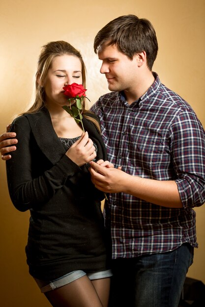 Schöne junge Frau, die rote Rose riecht, präsentiert von jungem Mann