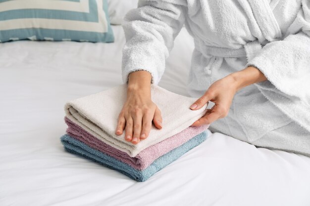 Schöne junge Frau, die saubere Handtücher auf Bett stapelt