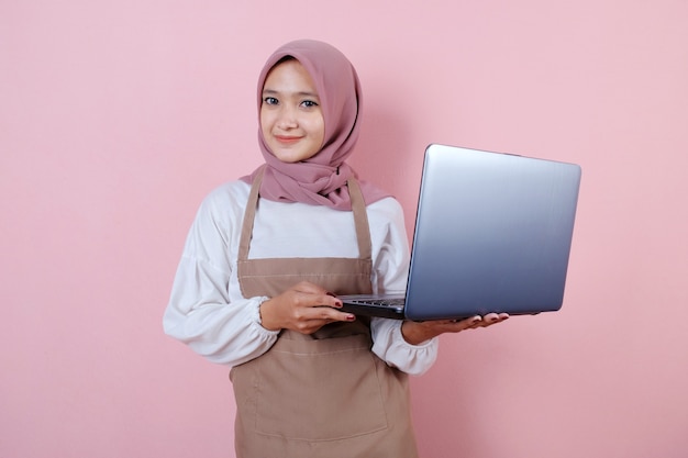 Schöne junge Frau, die Schürze mit Laptoplächeln und glücklich trägt