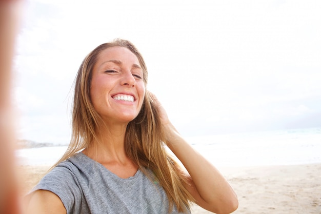 Schöne junge Frau, die selfie am Strand mit der Hand im Haar nimmt