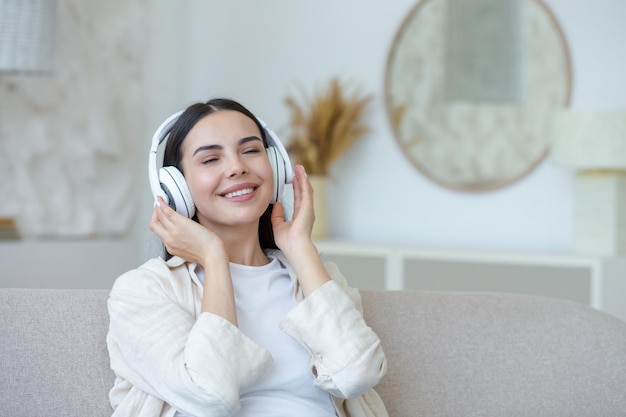 Schöne junge Frau, die sich ausruht und Musik in weißen großen Kopfhörern hört, die Brünette auf dem Sofa sitzt