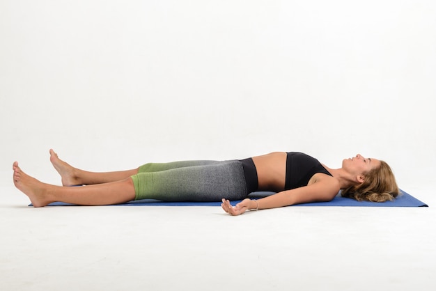 Schöne junge Frau, die Yoga auf weißer Wand - shavasana tut