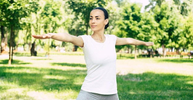 Schöne junge Frau, die Yoga im Park tut und wegschaut. Brünette Frau genießt die Natur bei einer Atemübung