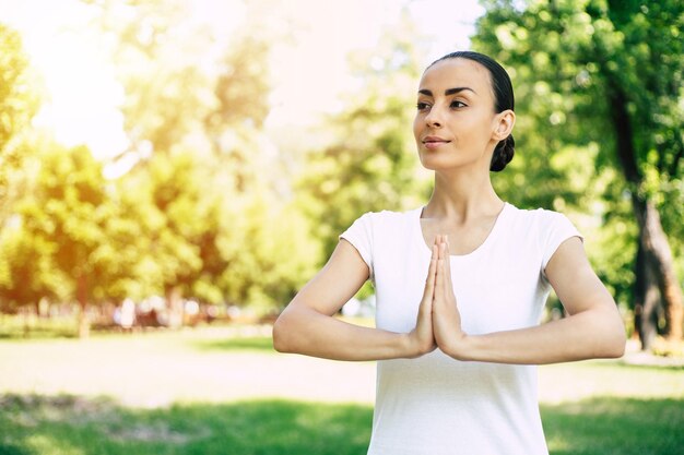 Schöne junge Frau, die Yoga im Park tut und wegschaut. Brünette Frau genießt die Natur bei einer Atemübung