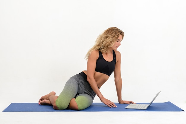 Schöne junge Frau, die Yoga mit Laptop auf Weiß tut