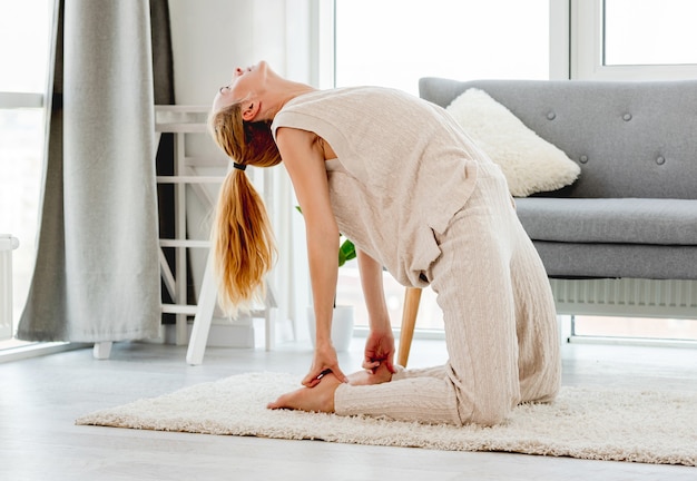 Schöne junge Frau, die Yogaübungen für Rückenflexibilität im sonnigen Raum macht