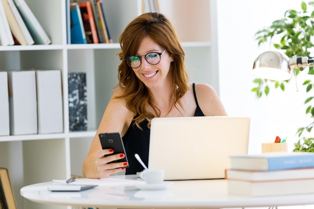 Schöne junge Frau, die zu Hause mit ihrem Laptop arbeitet.