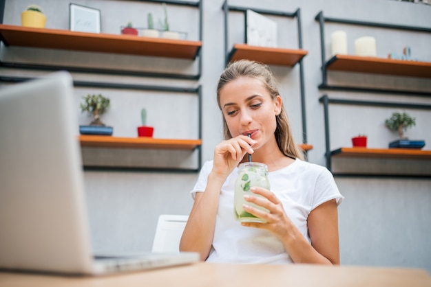 Schöne junge Frau, die zuhause frische Limonade trinkt.