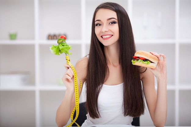 Schöne junge Frau, die zwischen gesundem Essen und Junk Food wählt