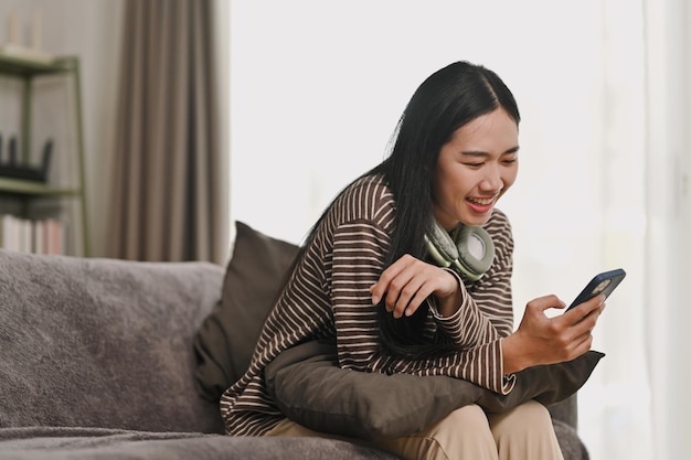 Schöne junge Frau entspannt sich auf dem Sofa und beobachtet soziale Medien auf ihrem Handy