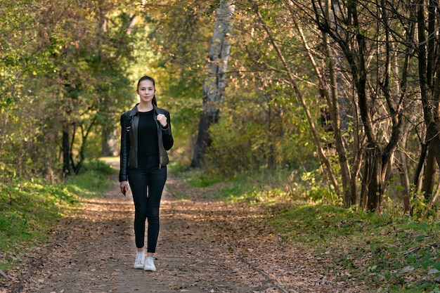 Schöne junge Frau geht in den Herbstpark. Glückliches Mädchen in schwarzer Kleidung im Wald. Gasse, Promenade.