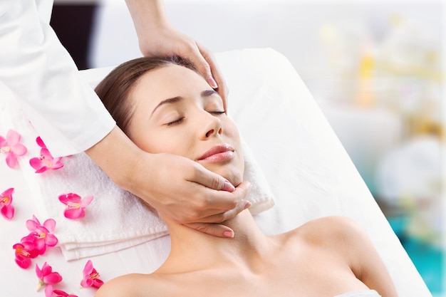 Schöne junge frau genießt gesichtsmassage im spa mit rosen, asiatische schönheit