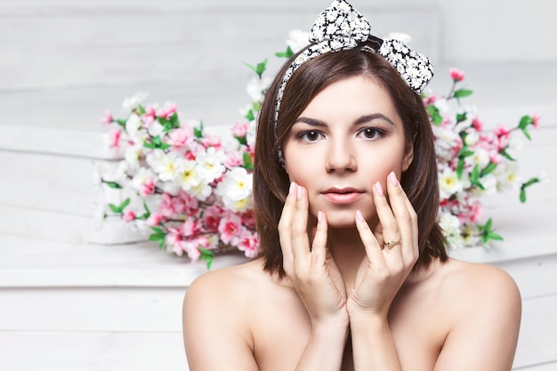 Schöne junge Frau Gesicht Nahaufnahme - perfekte Haut. Blumen Hintergrund .. Natürliche Maniküre. braune Augen