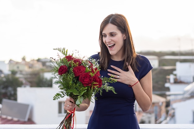 Schöne junge Frau glücklich und überrascht mit ihrem Blumenstrauß von roten Rosen