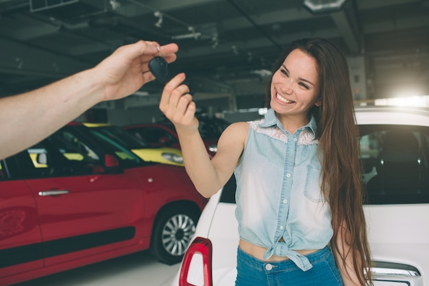 Schöne junge Frau hält einen Schlüssel im Autohaus