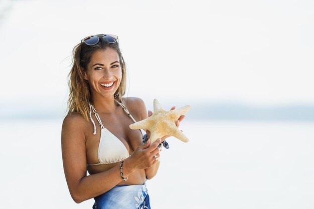 Schöne junge Frau hält Seesterne in der Hand und genießt den Strand. Blick in die Kamera.