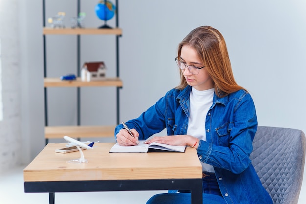 Schöne junge Frau im Büro, die Jeanskleidung trägt, machen Sie einige Notizen auf Notizbuch.