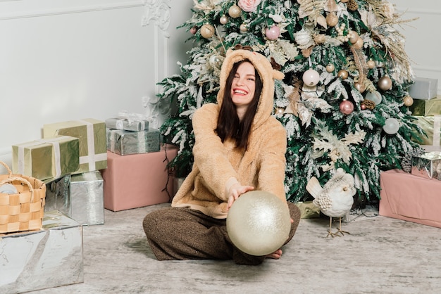 Schöne junge Frau im eleganten Kleid, das nahe bei Weihnachtsbaum und Geschenken steht.