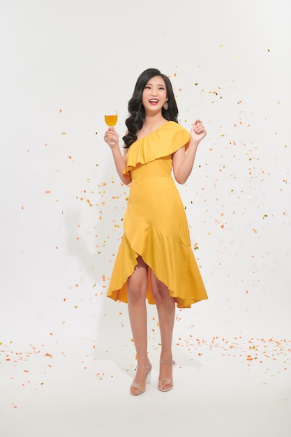 Schöne junge Frau im gelben Kleid feiert mit einem Glas Champagner und Konfetti