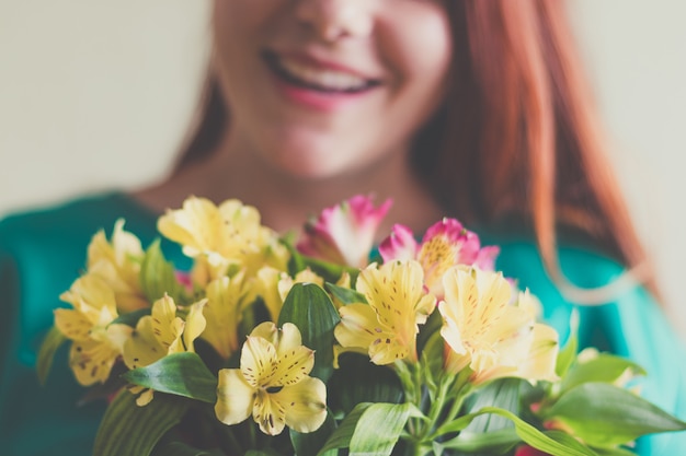 Schöne junge frau im grünen kleid, das frühlingsblumenblumenstrauß hält