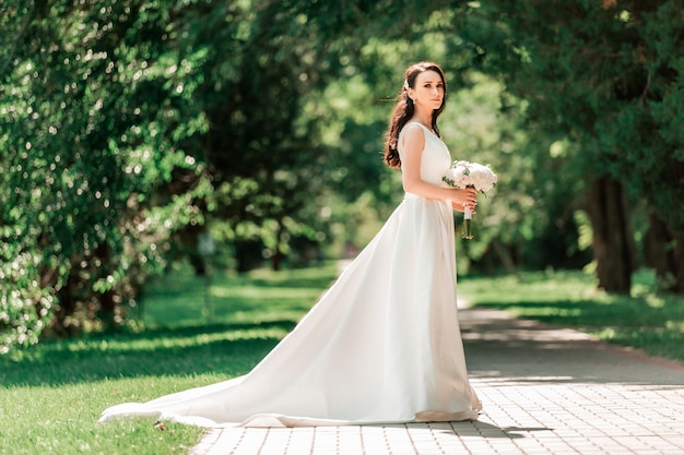 Schöne junge Frau im Hochzeitskleid, die im Park steht