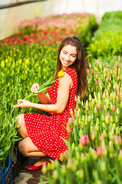 Schöne junge Frau im Kleid, das bei Sonnenuntergang in einem roten Tulpenfeld sitzt.