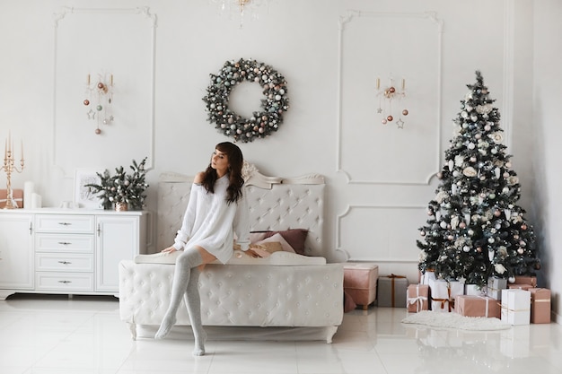 Schöne junge Frau im kuscheligen Pullover, der zu Hause Interieur für Weihnachten dekoriert aufwirft.