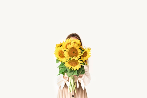 Schöne junge Frau im Leinenkleid, das Sonnenblumenstrauß auf Weiß hält