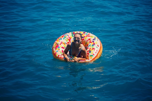 Schöne junge Frau im Meer schwimmt auf einem aufblasbaren Ring und hat Spaß im Urlaub Mädchen in einem hellen Badeanzug am Meer unter dem Sonnenlicht