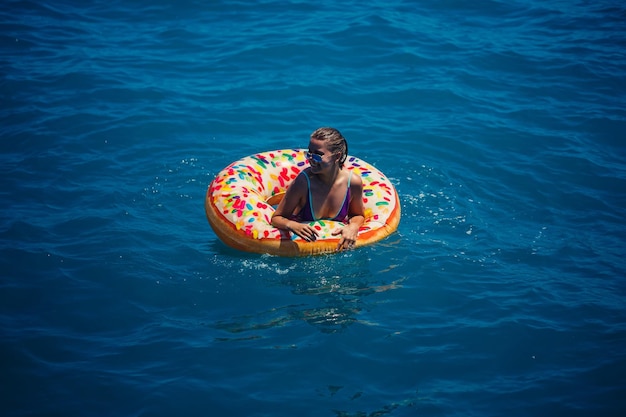 Schöne junge Frau im Meer schwimmt auf einem aufblasbaren Ring und hat Spaß im Urlaub Mädchen in einem hellen Badeanzug am Meer unter dem Sonnenlicht
