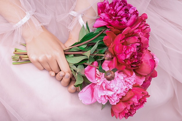 Schöne junge Frau im rosa Kleid, die Pfingstrosenblumenstrauß in ihren Händen hält