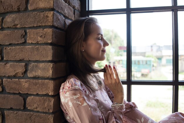 Foto schöne junge frau im rosa kleid sitzt auf der fensterbank