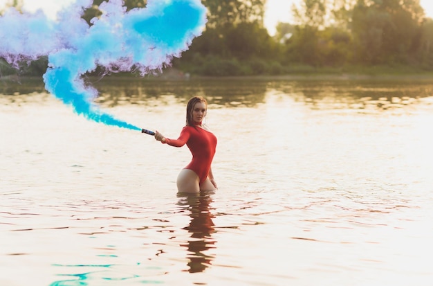 Schöne junge Frau im roten Badeanzug posiert in der Nähe des Flusses Sommer-Lifestyle-Rauchbombe