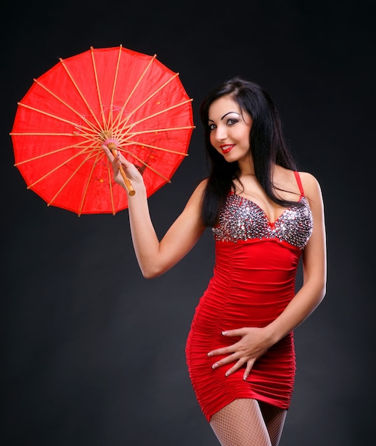 Schöne junge Frau im roten Kleid mit rotem chinesischem Regenschirm auf dunklem Hintergrund