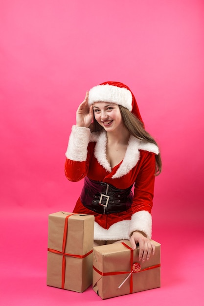 Schöne junge Frau im Weihnachtsmann-Kostüm vor dem roten Hintergrund.