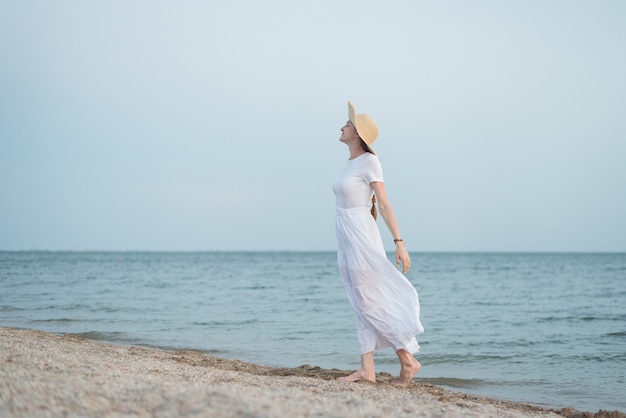 Schöne junge Frau im weißen Kleid und im Hut am Strand. Aristokratin am Meer
